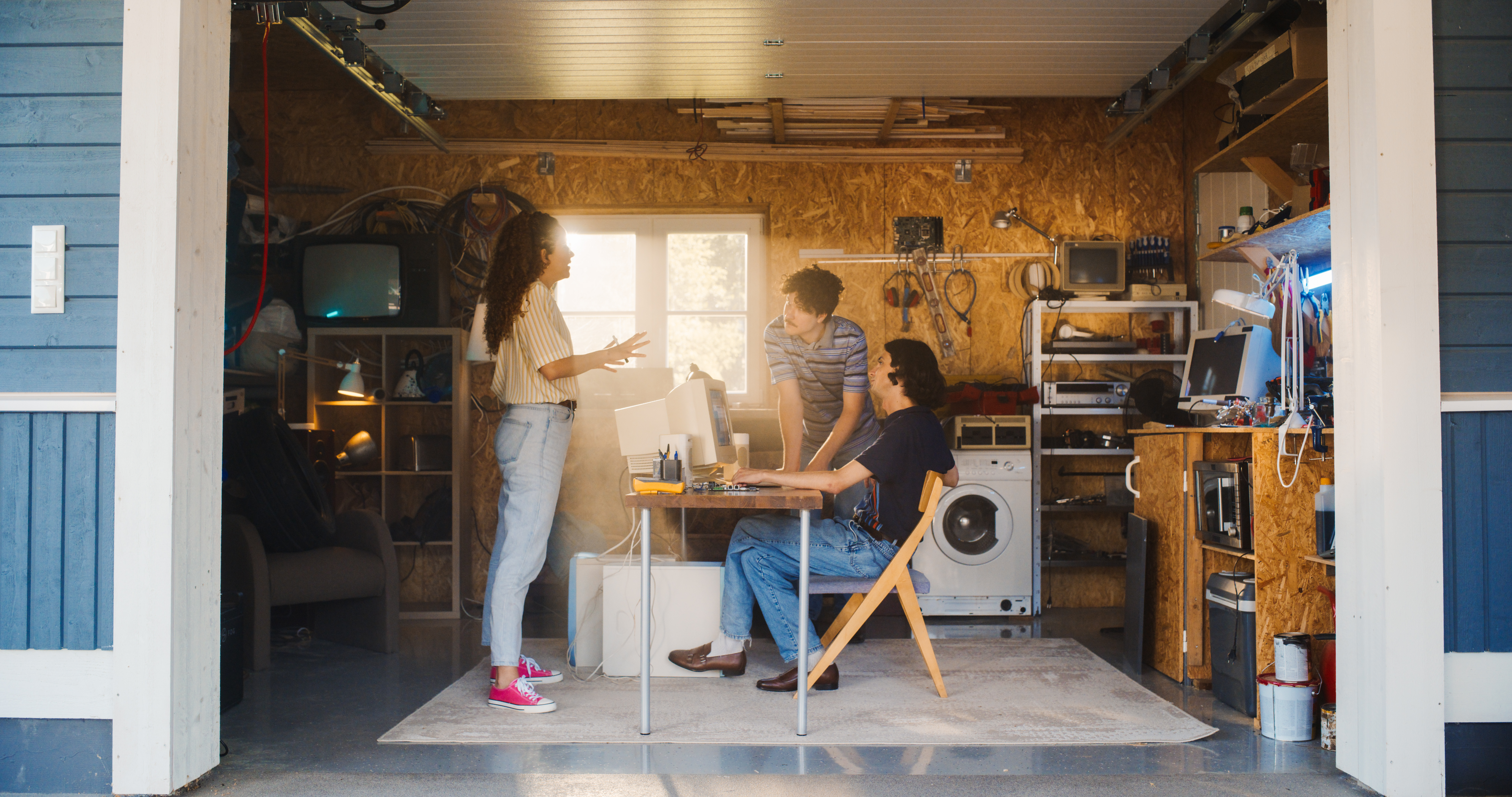 Diverse Team Of Three Young Tech Startup Company Founders Working In Retro Garage, Using Old Desktop Computer. Male And Female Entrepreneurs Developing Innovative Online Service In Nostalgic Nineties.